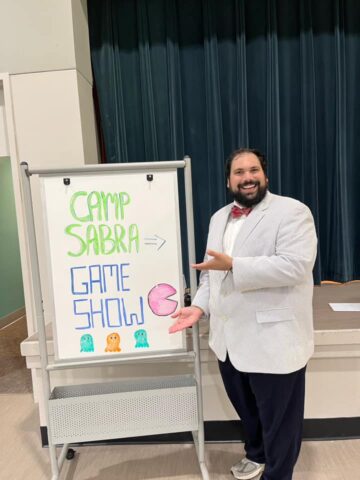 A man in a suit standing next to a sign that says camp sabra.