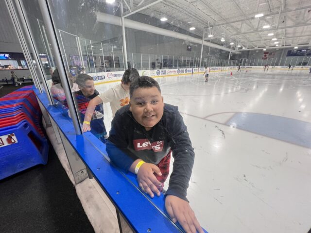 A young boy is leaning over the edge of an ice rink.