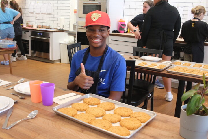 A young boy giving a thumbs up in front of a tray of cookies.