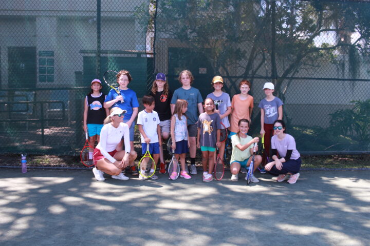 A group of children posing for a picture on a tennis court.