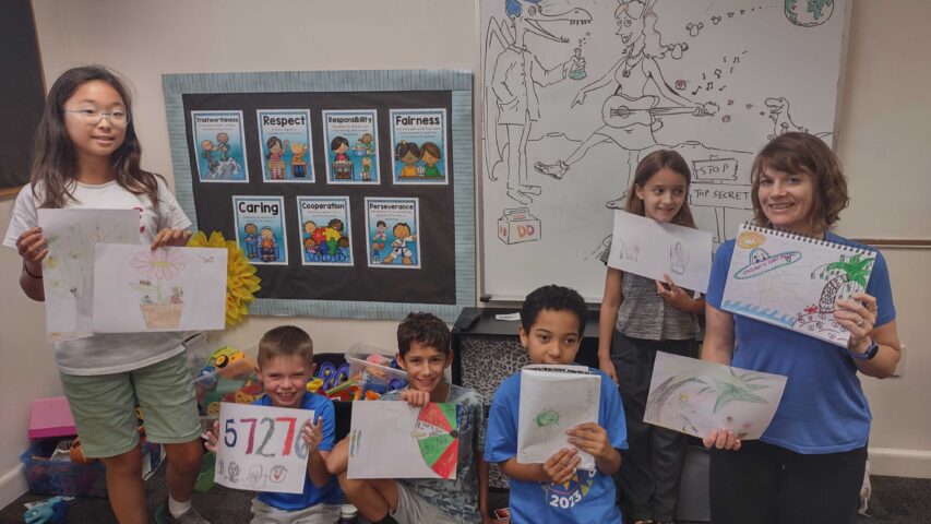 A group of children holding up drawings in a classroom.