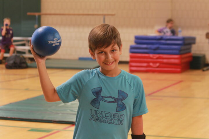 A young boy holding a blue ball in a gym.