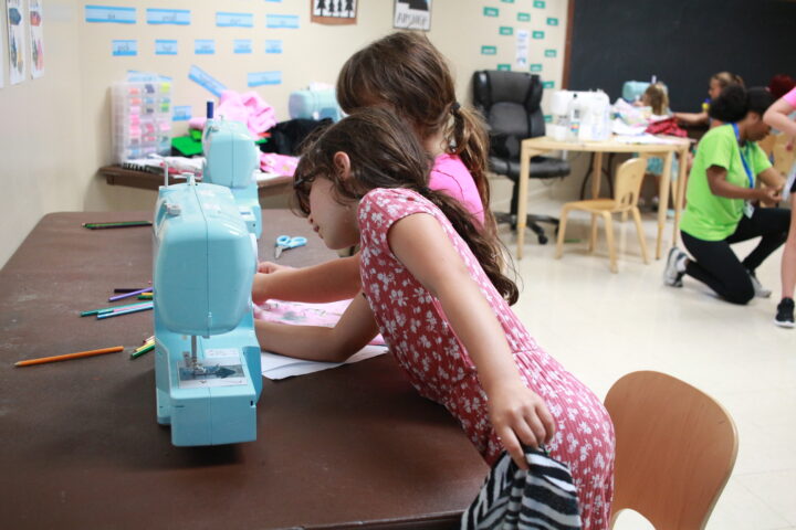 Two girls working on a sewing machine in a classroom.