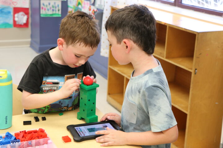 Two young boys playing with a tablet in a classroom.