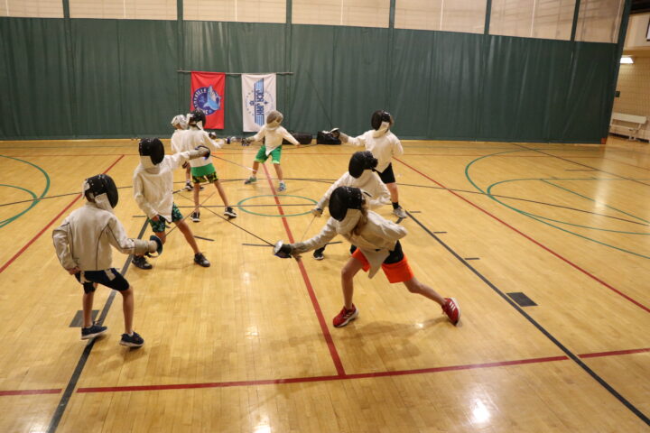 A group of kids fencing in a gym.