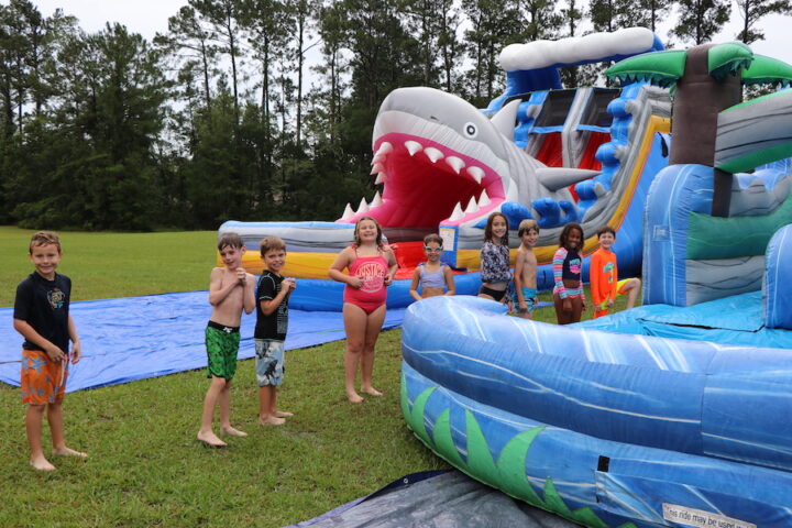 A group of kids standing in front of an inflatable shark slide.