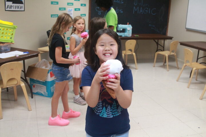 A young girl holding a pink ice cream cone in a classroom.
