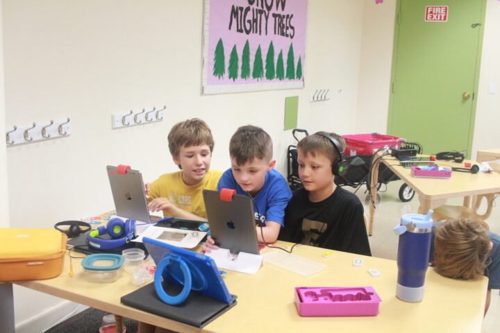 A group of boys are sitting at a table with laptops.