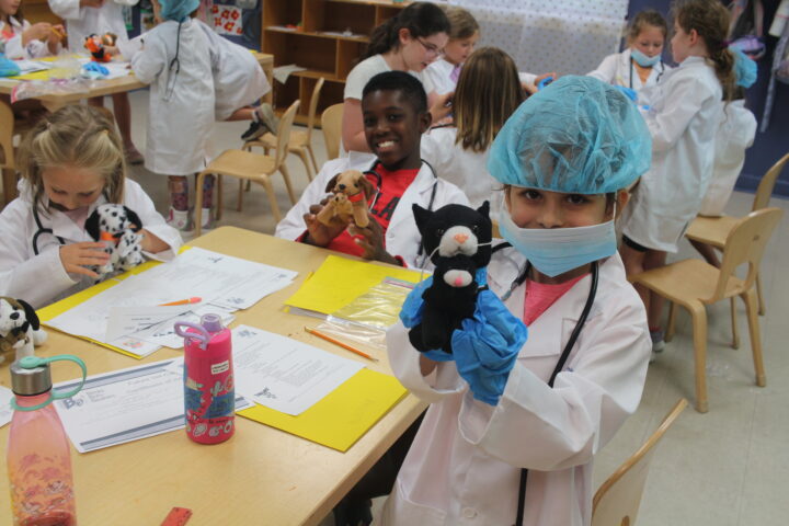 A group of children in lab coats holding stuffed animals.