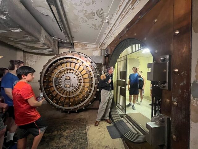A group of people standing in front of a large bank vault.
