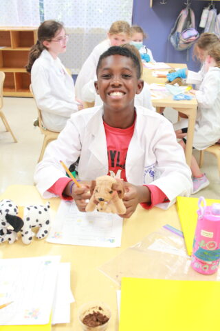 A boy in a lab coat holding a stuffed animal.