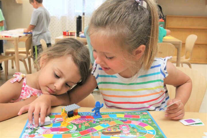 Two young girls playing a board game in a classroom.