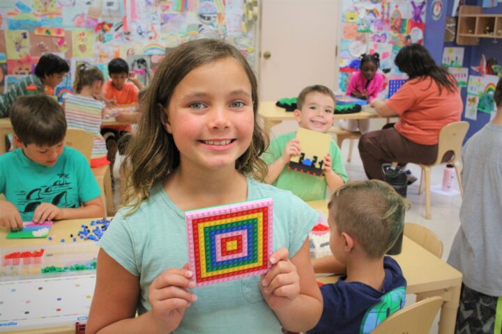 A young girl holding up a bead square in a classroom.