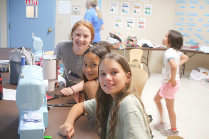 A group of girls sitting at a table with a sewing machine.
