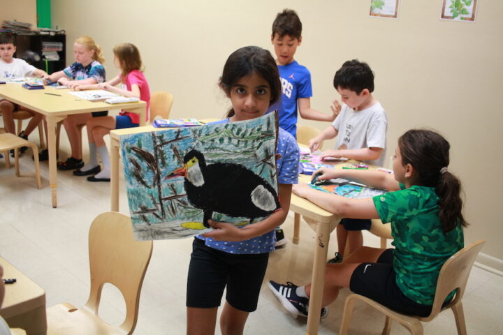 A group of children in a classroom painting a picture of a bird.
