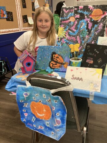 A young girl standing in front of a table full of art work.