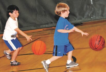 Two young boys playing basketball on a gym floor.