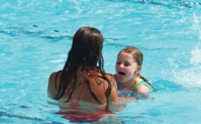 A young girl is swimming with a woman in a pool.