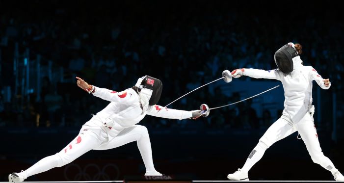 Two fencers in a fencing match at night.