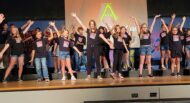 A group of children on stage with their hands raised.