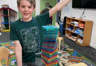 A boy is standing in front of a stack of colorful blocks.