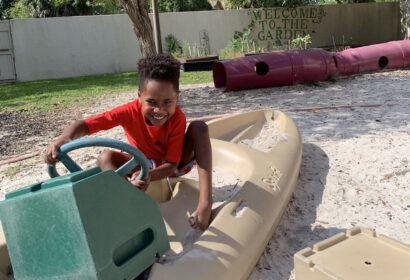 A young boy playing with a boat in the sand.