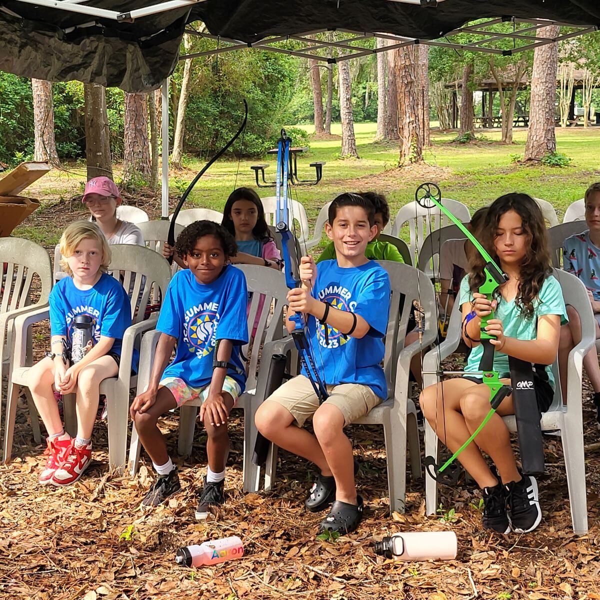 A group of children sitting in chairs under a tent.