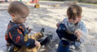 Two toddlers playing in the sand at a playground.