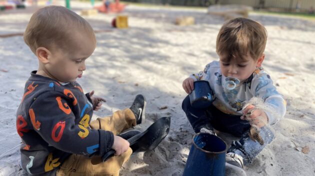 Two toddlers playing in the sand at a playground.