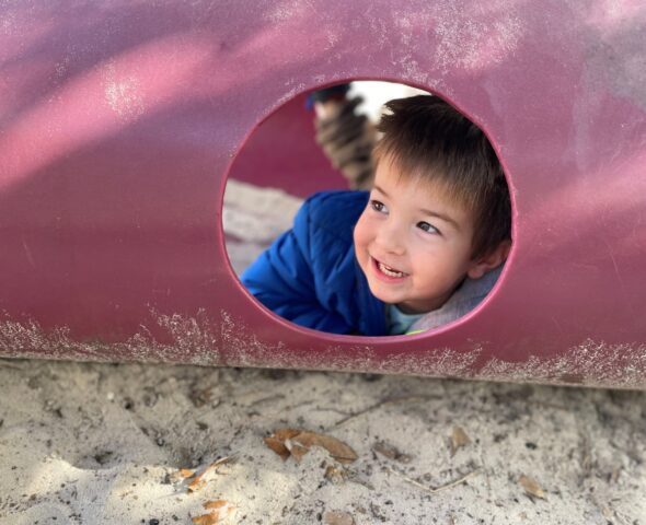 A young boy peeking out of a play structure.