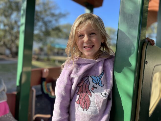 A little girl wearing a unicorn sweatshirt on a playground.