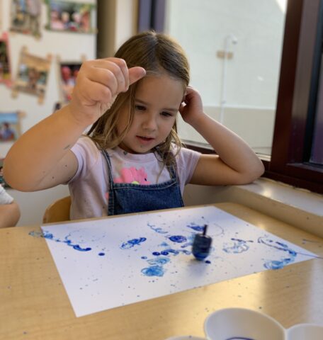 A little girl is painting with blue paint on a piece of paper.