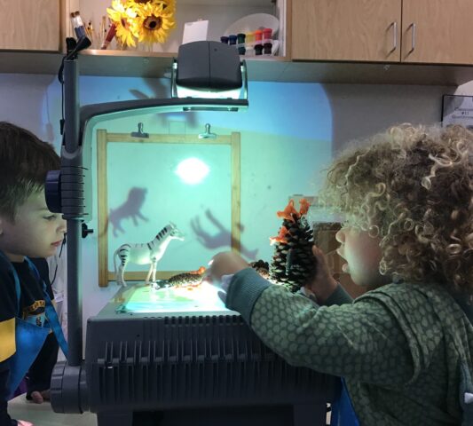 Two children playing with a projector in a classroom.