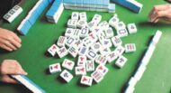 A Mahjong game in progress with three hands visible, tiles arranged on a green playing mat and some scattered in the center.