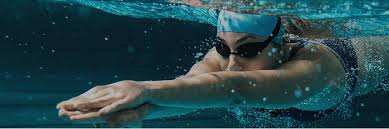 An underwater view of a person swimming with their arms extended forward, wearing goggles and a swim cap, against a blurry aquatic background.