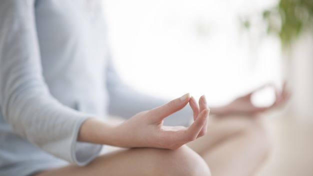 Person sitting cross-legged in a meditative posture with their hands resting on their knees, forming a mudra gesture.