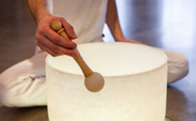 A person in white clothing uses a mallet to play a white singing bowl.