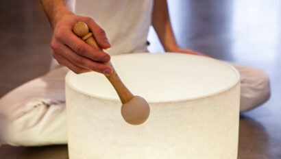 A person in white clothing uses a mallet to play a white singing bowl.