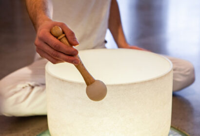 A person in white clothing uses a mallet to play a white singing bowl.