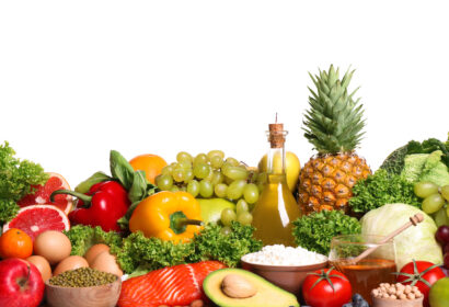 A variety of fresh fruits, vegetables, salmon, eggs, olive oil, and other healthy foods are arranged in a colorful display against a white background.