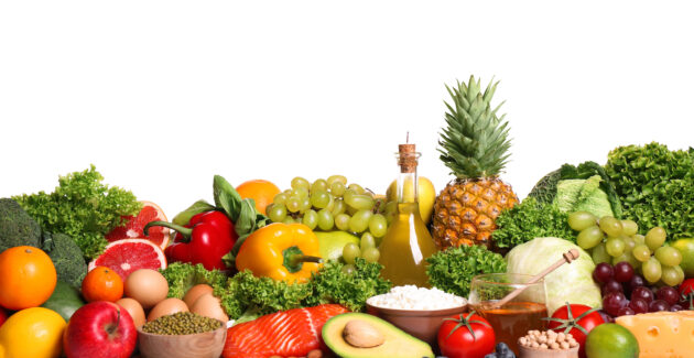 A variety of fresh fruits, vegetables, salmon, eggs, olive oil, and other healthy foods are arranged in a colorful display against a white background.