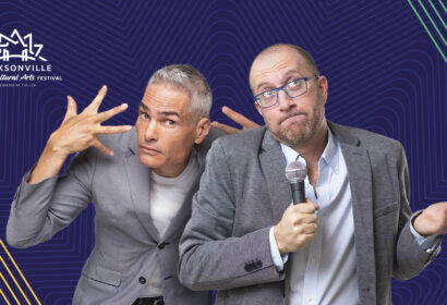 Two men in suits, one with grey hair making expressive hand gestures and the other bald with glasses holding a microphone, stand in front of a blue background with the Jacksonville Jewish Cultural Arts Festival logo.