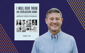 A man in a checkered shirt stands smiling in front of a book titled "I Will Give Them an Everlasting Name: Jacksonville's Stories of the Holocaust" by Samuel Cox, displayed against a blue patterned background.