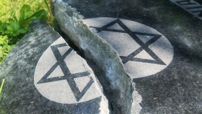 A cracked gravestone with a Star of David symbol, surrounded by grass.