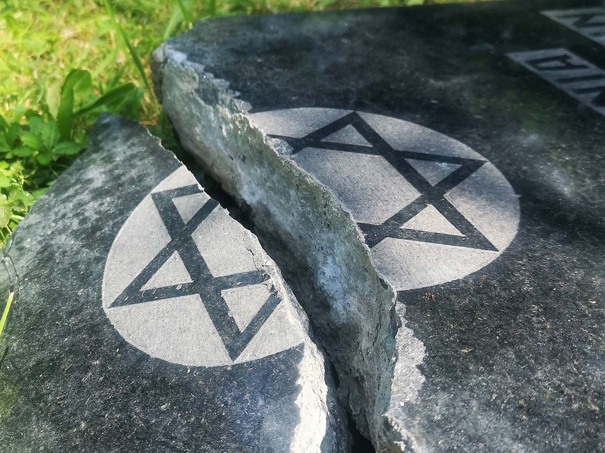 A cracked gravestone with a Star of David symbol, surrounded by grass.