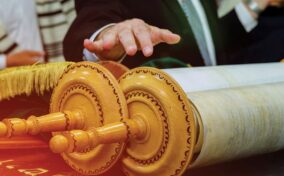 A person reaching towards an open Torah scroll, which is placed on a table.