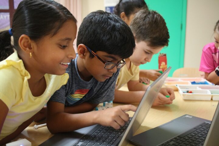 Children gathered around laptops, focusing intently on their screens while collaborating.