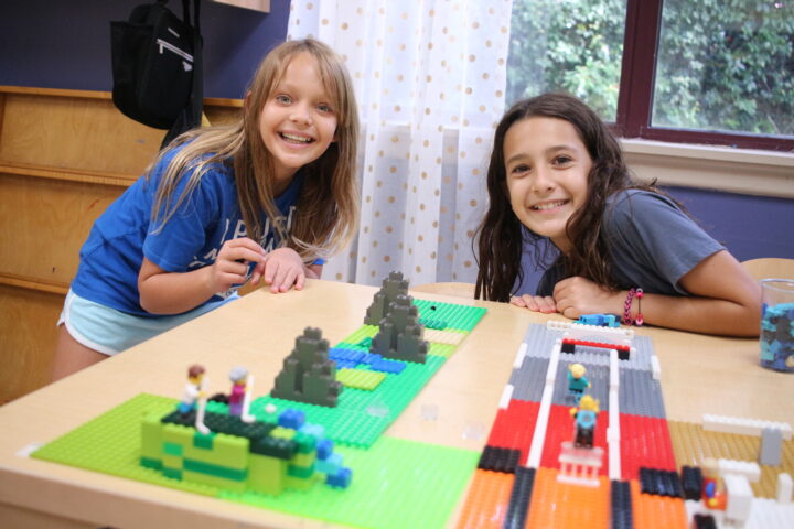 Two kids smiling while playing with LEGO sets on a table.