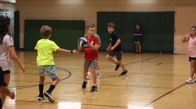 Children playing basketball in a gymnasium, with one child passing the ball.