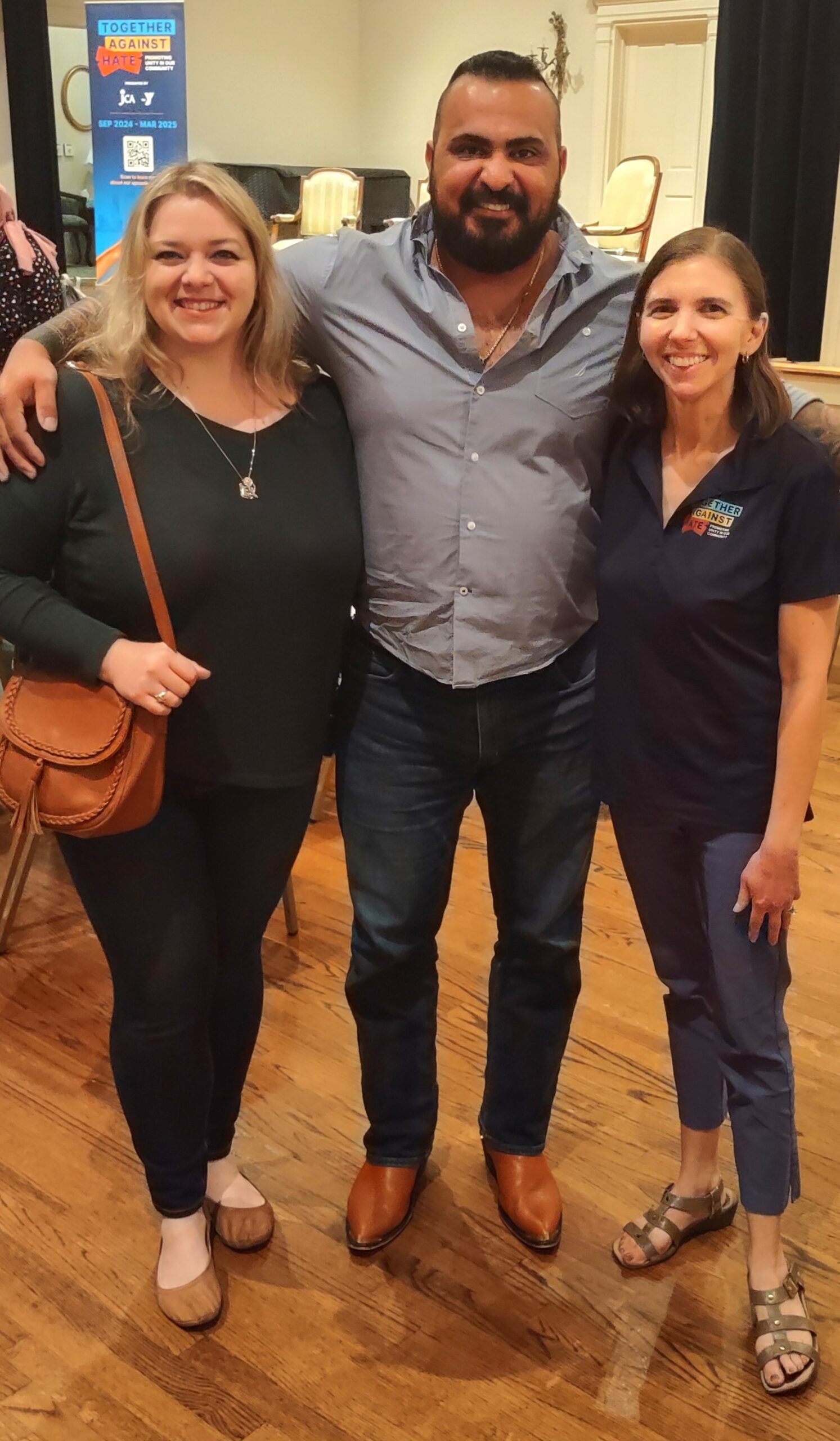 Three people standing together indoors, smiling at the camera.